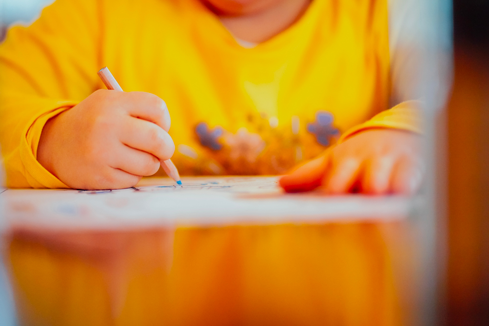 jeune enfant en train de colorier avec un crayon de couleur